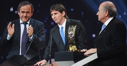 Messi houidt een toespraak, geflankeerd door Platini en Blatter