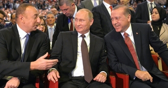 Alijev praat tegen een geamuseerde Poetin en Erdogan, terwijl ze in het publiek zitten