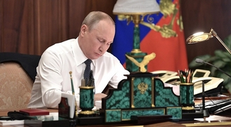 vóór de ceremonie zit Poetin in hemdsmouwen achter zijn bureau